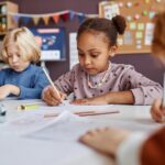 Cute African American schoolgirl drawing among her classmates