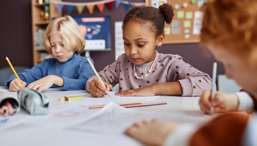 Cute African American schoolgirl drawing among her classmates