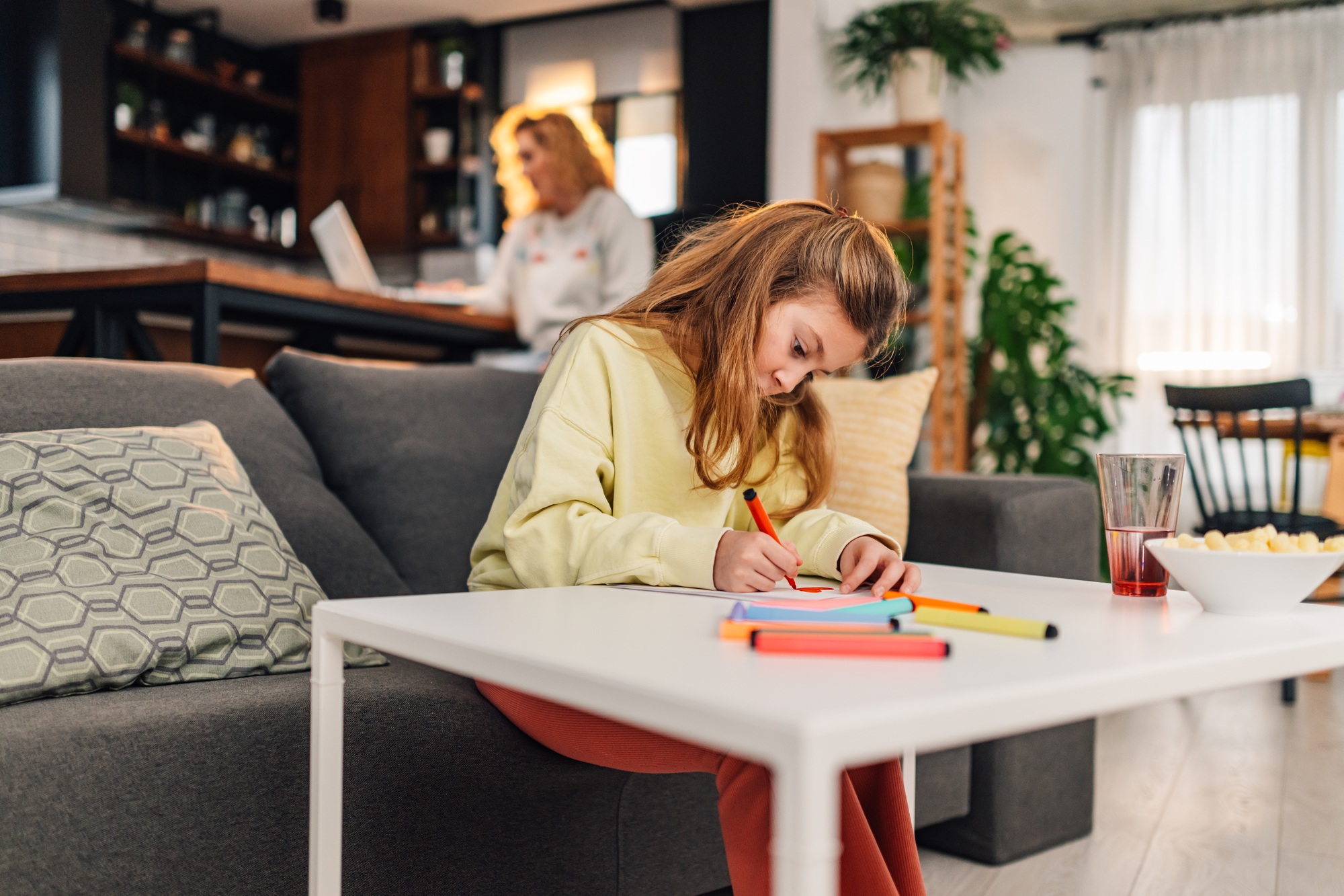 Cute child drawing a greeting card for mother's day while mother is working on laptop