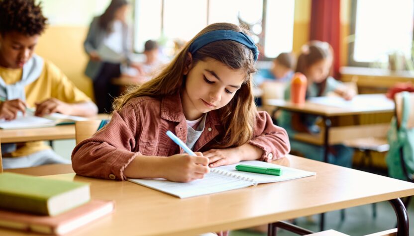 Elementary student writing in her notebook on a class at school.