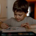 The boy draws a drawing with watercolor paints at home
