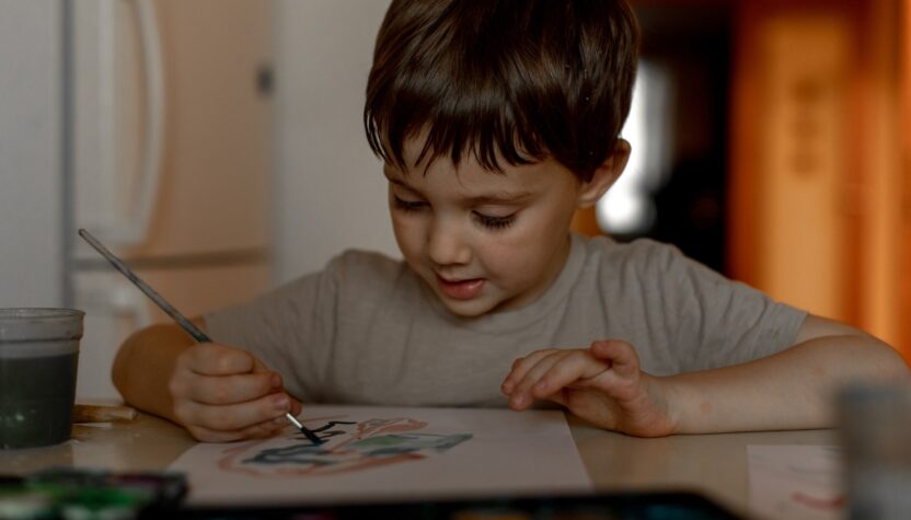 The boy draws a drawing with watercolor paints at home
