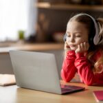 E-Learning Problems. Bored Little Girl In Wireless Headphones Looking At Laptop Screen