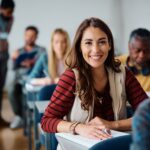 Happy female student learning in the classroom and looking at camera.