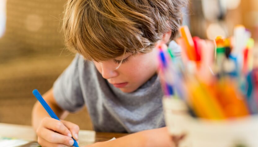 6 year old boy drawing amoung colorful pens
