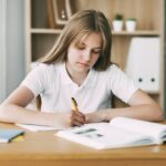 A high school student takes notes from a book, a teenage girl does her homework
