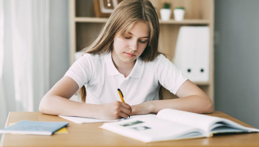 A high school student takes notes from a book, a teenage girl does her homework