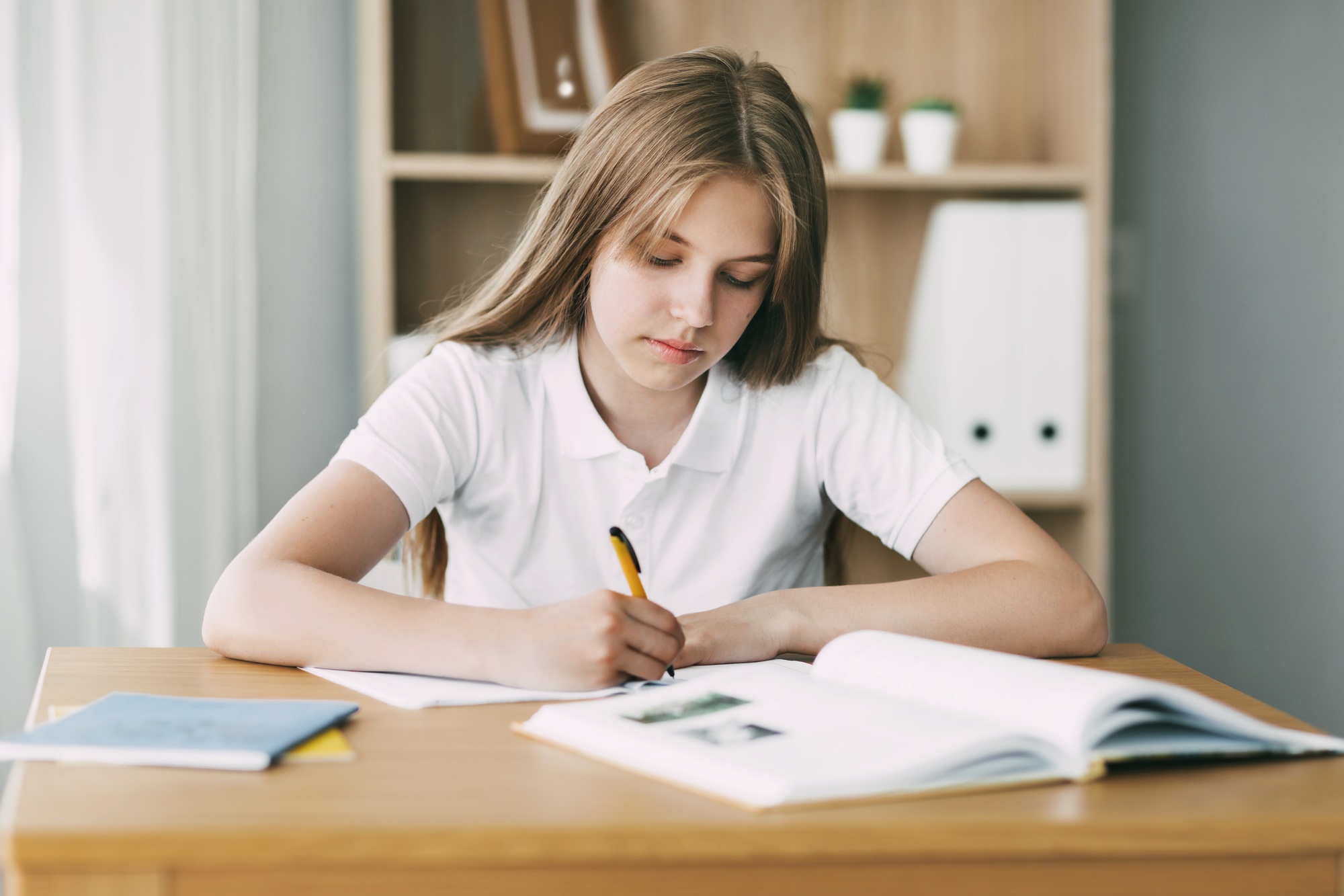 A high school student takes notes from a book, a teenage girl does her homework