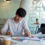 Asian man designer is drawing, creating a sample design using a color sample tablet at the office.