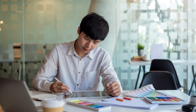 Asian man designer is drawing, creating a sample design using a color sample tablet at the office.