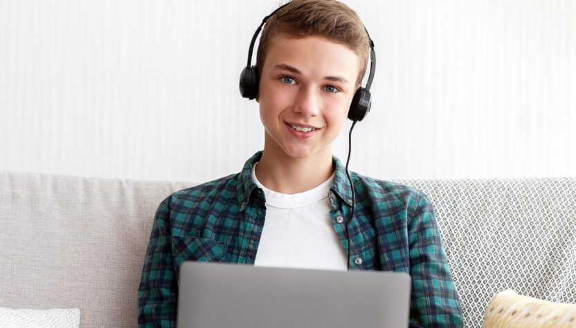 Cheerful teen boy with headset playing games on laptop