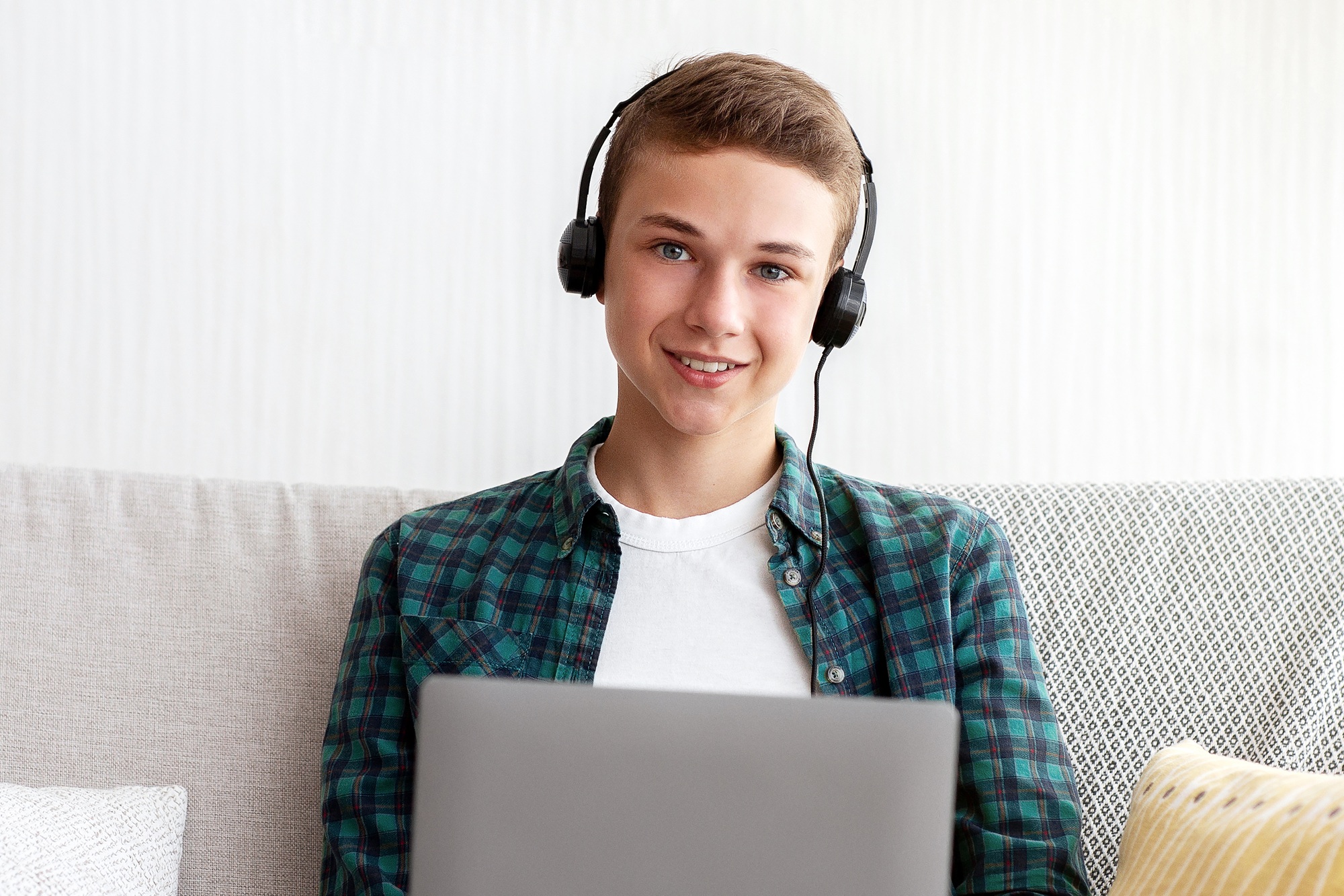 Cheerful teen boy with headset playing games on laptop