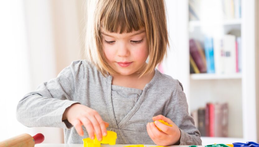 Little girl cutting out yellow modeling clay