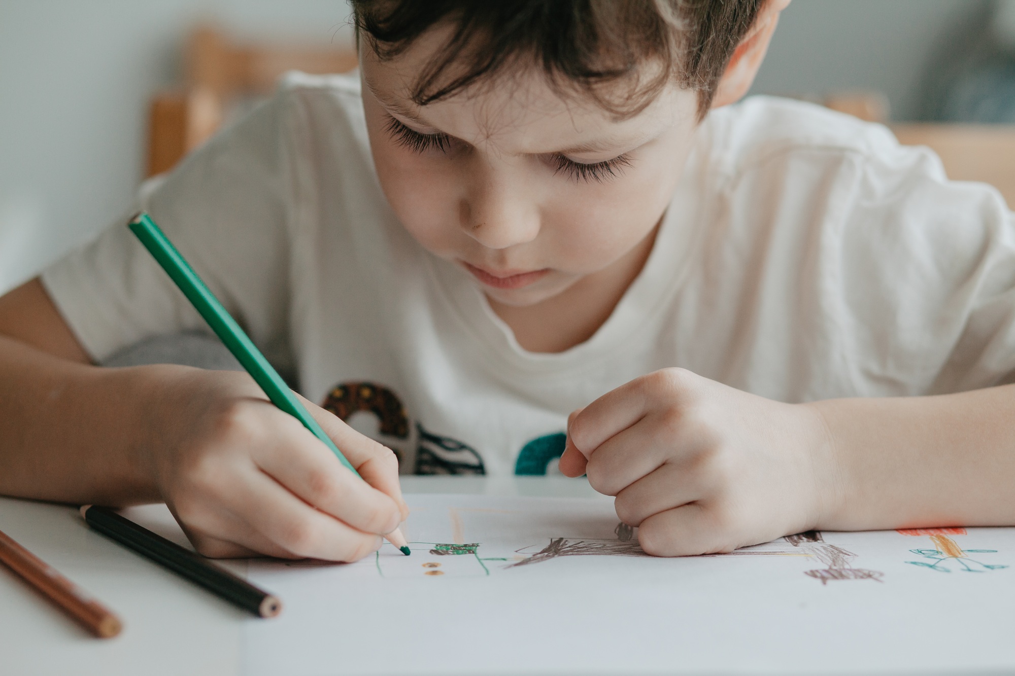 The boy draws with pencils at the kitchen, closeup