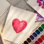Watercolor drawing heart, palette, brushes in the sun.